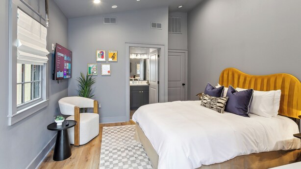 Un dormitorio moderno con una cama grande, una mesita de noche, una silla y una pequeña mesa con una planta.