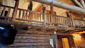 L’intérieur d’un chalet en bois doté d’un balcon, de poutres apparentes et d’une esthétique rustique.