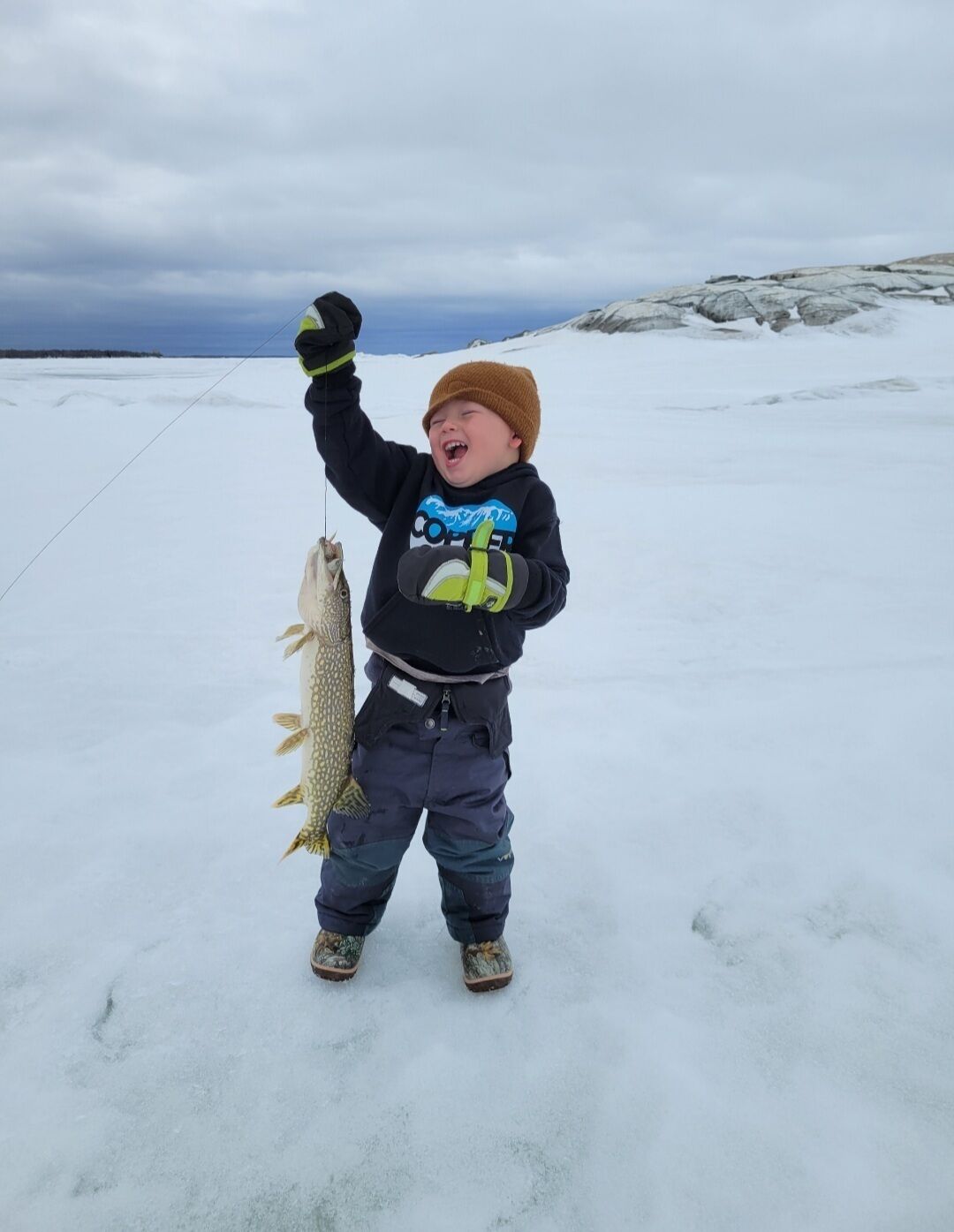 Un niño sosteniendo un pez en un paisaje nevado.