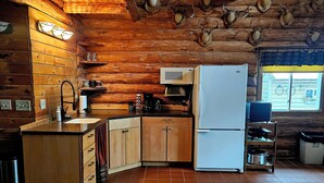 Une cuisine rustique avec des murs en bois, un sol carrelé, un réfrigérateur blanc, un four à micro-ondes et une machine à café.