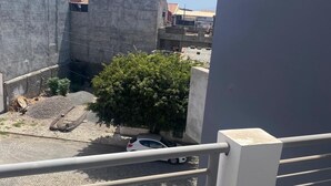 Un balcon donnant sur une cour, une voiture garée et des bâtiments aux toits recouverts de tuiles rouges.
