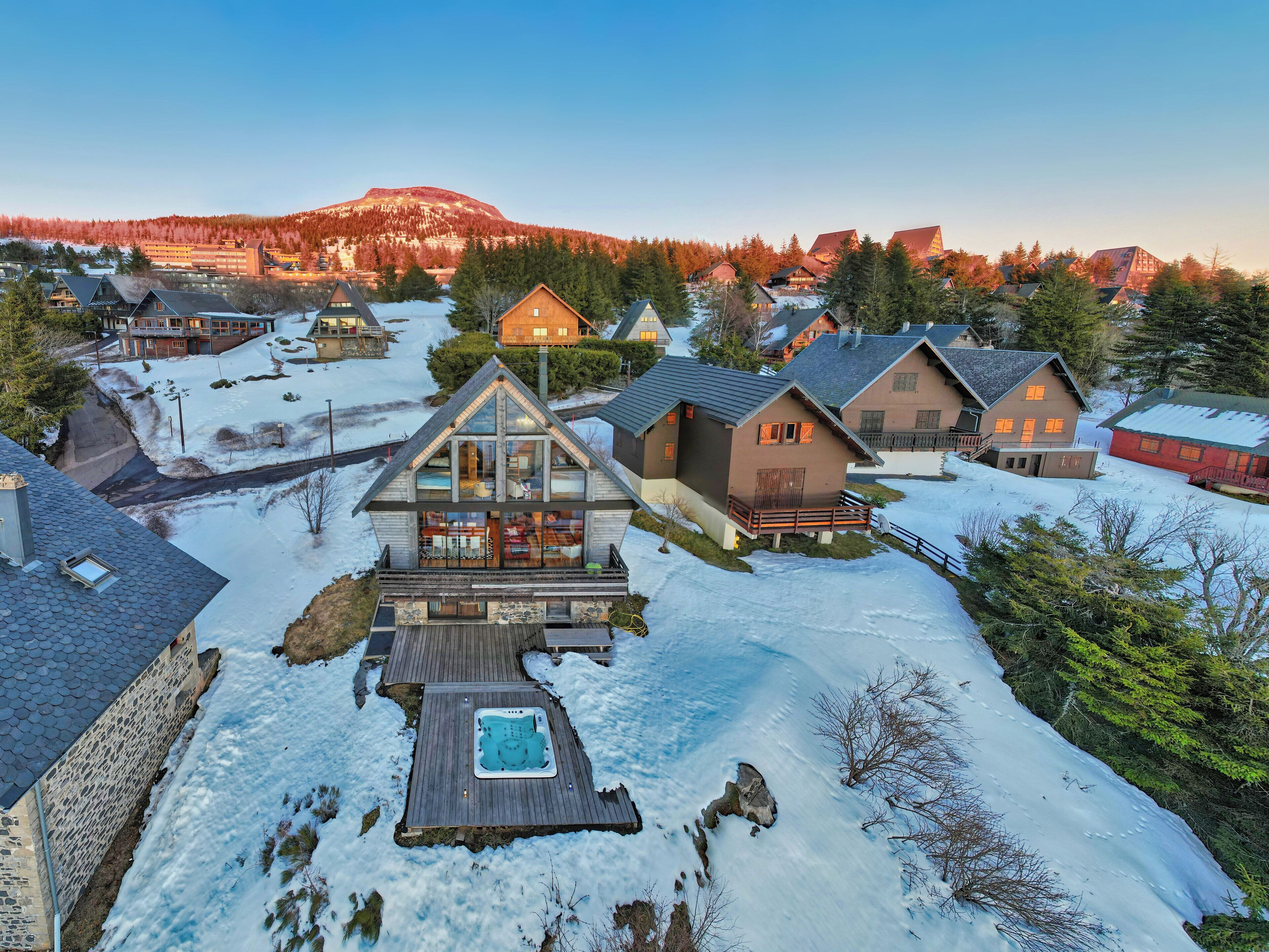 Zona residencial nevada con casas, un muelle de madera y un jacuzzi.