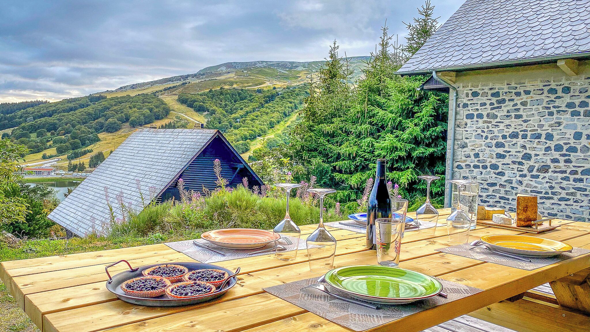 A wooden table set outdoors with a scenic view of hills and a stone building.