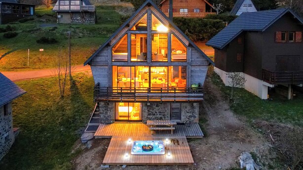 Una cabaña de madera con balcón, jacuzzi y cimientos de piedra.