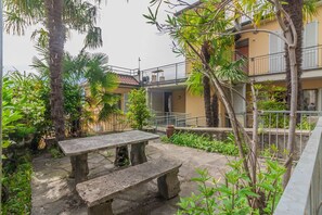 Un patio con un banco de piedra, palmeras y un edificio con balcones.