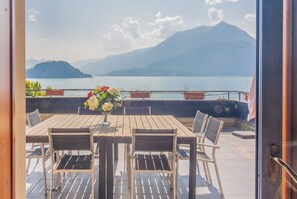 Une table en bois, entourée de chaises, et un vase de fleurs, le tout placé devant un lac avec des montagnes en arrière-plan.