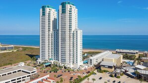 A high-rise hotel with multiple floors, a parking area, and a view of the ocean.