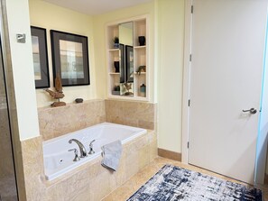 Une salle de bain moderne avec une grande baignoire, des carreaux de marbre, un porte-serviettes, un miroir et une étagère ornée d’objets décoratifs.