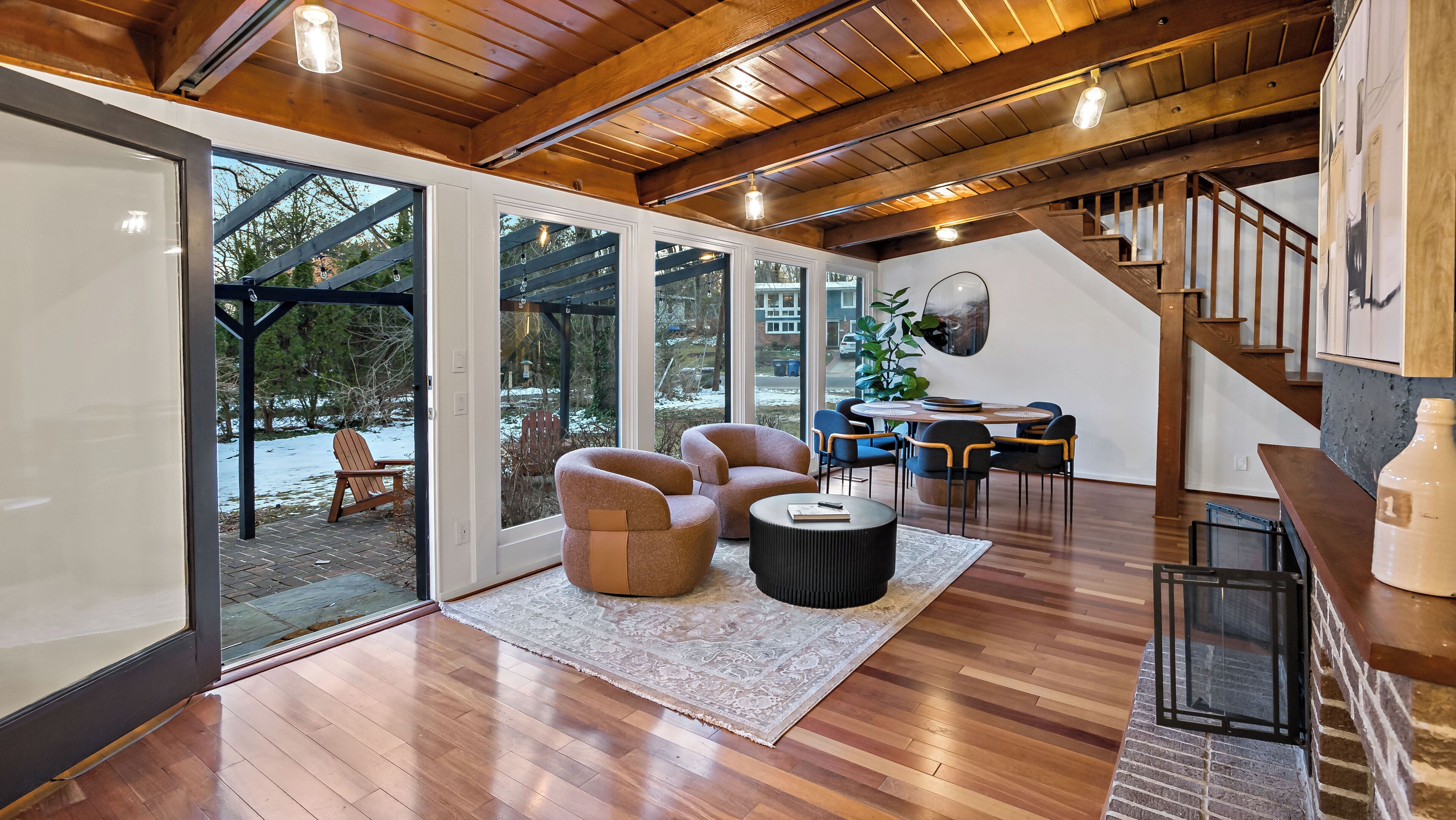 A spacious living area with a wooden floor, large windows, and a staircase leading to an upper level.