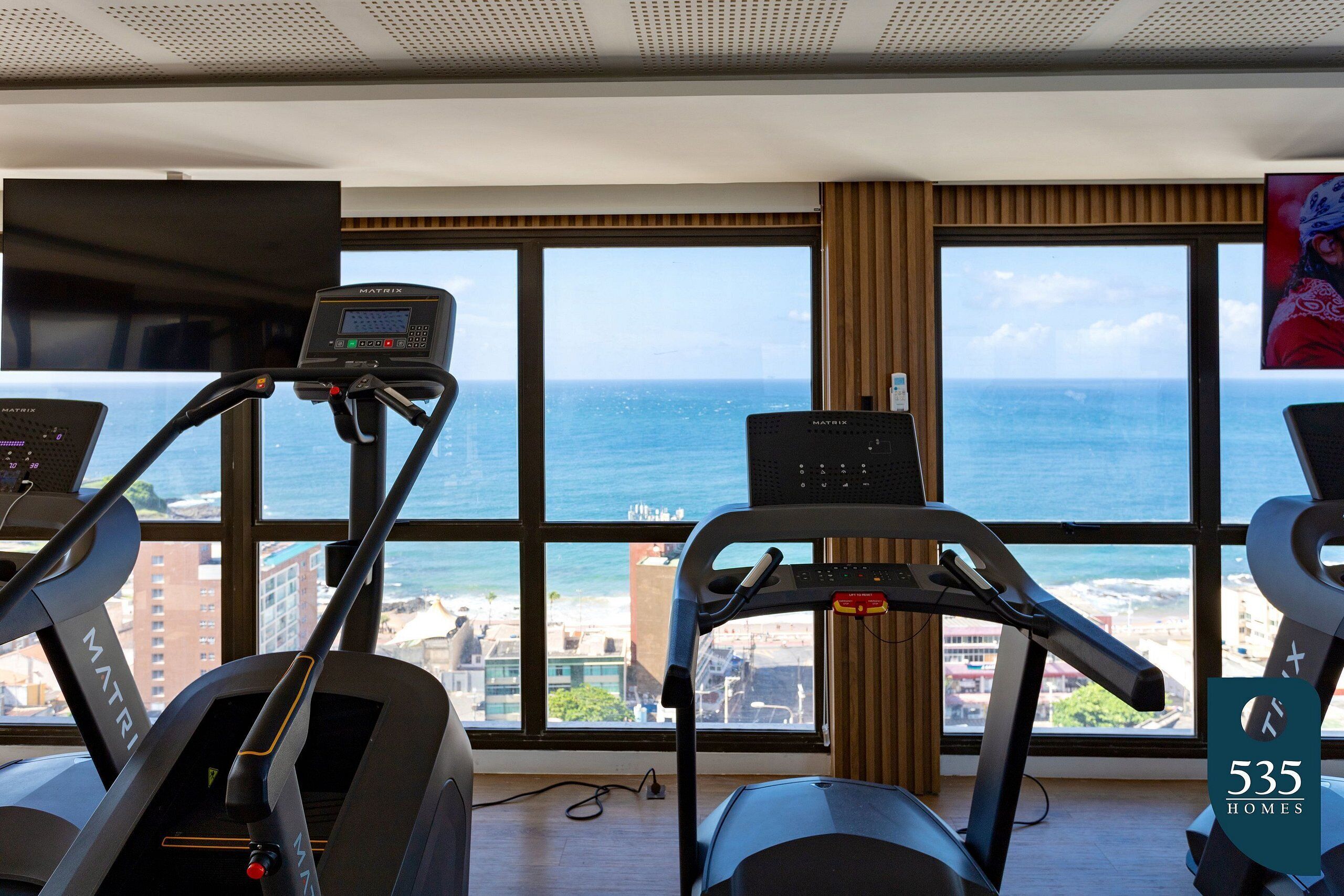 Une salle de sport équipée de tapis de course et dotée d’une grande fenêtre donnant sur l’océan.