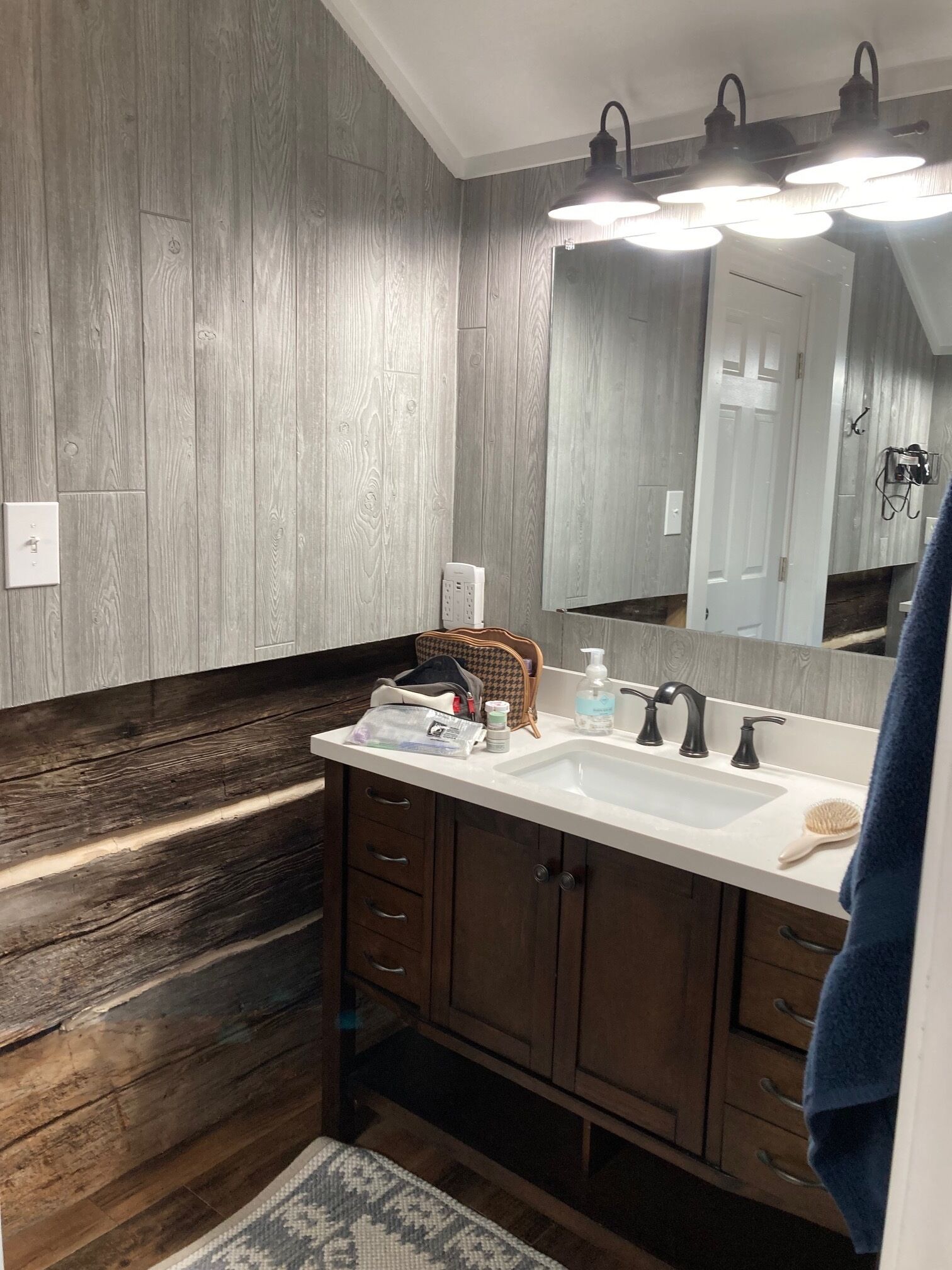 Un baño con suelo de madera, un lavamanos blanco, armarios de madera oscura y un espejo con luces arriba.