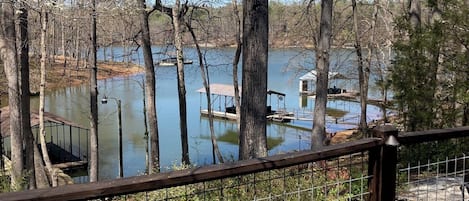 A wooden deck with a metal railing overlooking a lake with boats and a dock.