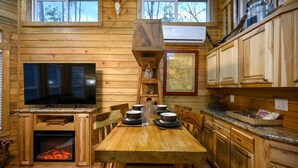 Interior de una cabaña de madera con una mesa de comedor, sillas, chimenea, televisor y armarios de madera.