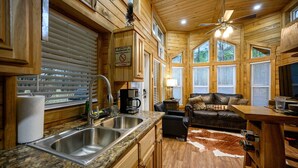 Interior de una cabaña de madera con cocina, comedor y un sofá de cuero.