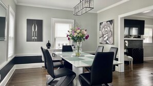 A modern dining room with a rectangular table, black chairs, a vase with flowers, and artwork on the walls.