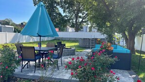 A patio with a table and chairs, a blue umbrella, and a blue sofa.