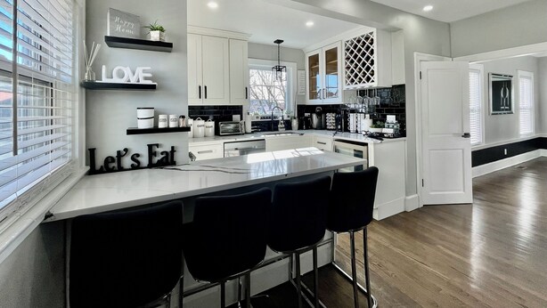 A modern kitchen with a central island, bar stools, and a 'Let's Eat' sign.