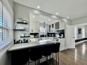 Una cocina moderna con una isla central, taburetes de bar y un letrero que dice 'Let's Eat'.