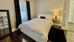 A neatly made bed with white linens, a bedside lamp, and a black rug on a wooden floor.