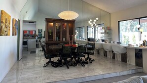 A modern dining area with a marble floor, a wooden dining table with ornate chairs, a large cabinet with glass doors, and a pendant light. - Tranquil 3-bedroom house in Palm Springs with WiFi and AC (Palm Springs)