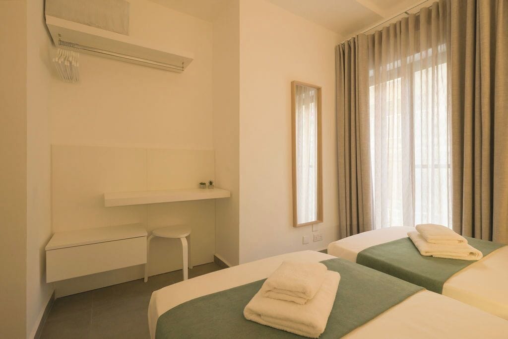 Ein Hotelzimmer mit zwei Betten, einem Schreibtisch, einem Stuhl, einem Spiegel und einem Fenster mit Vorhängen.