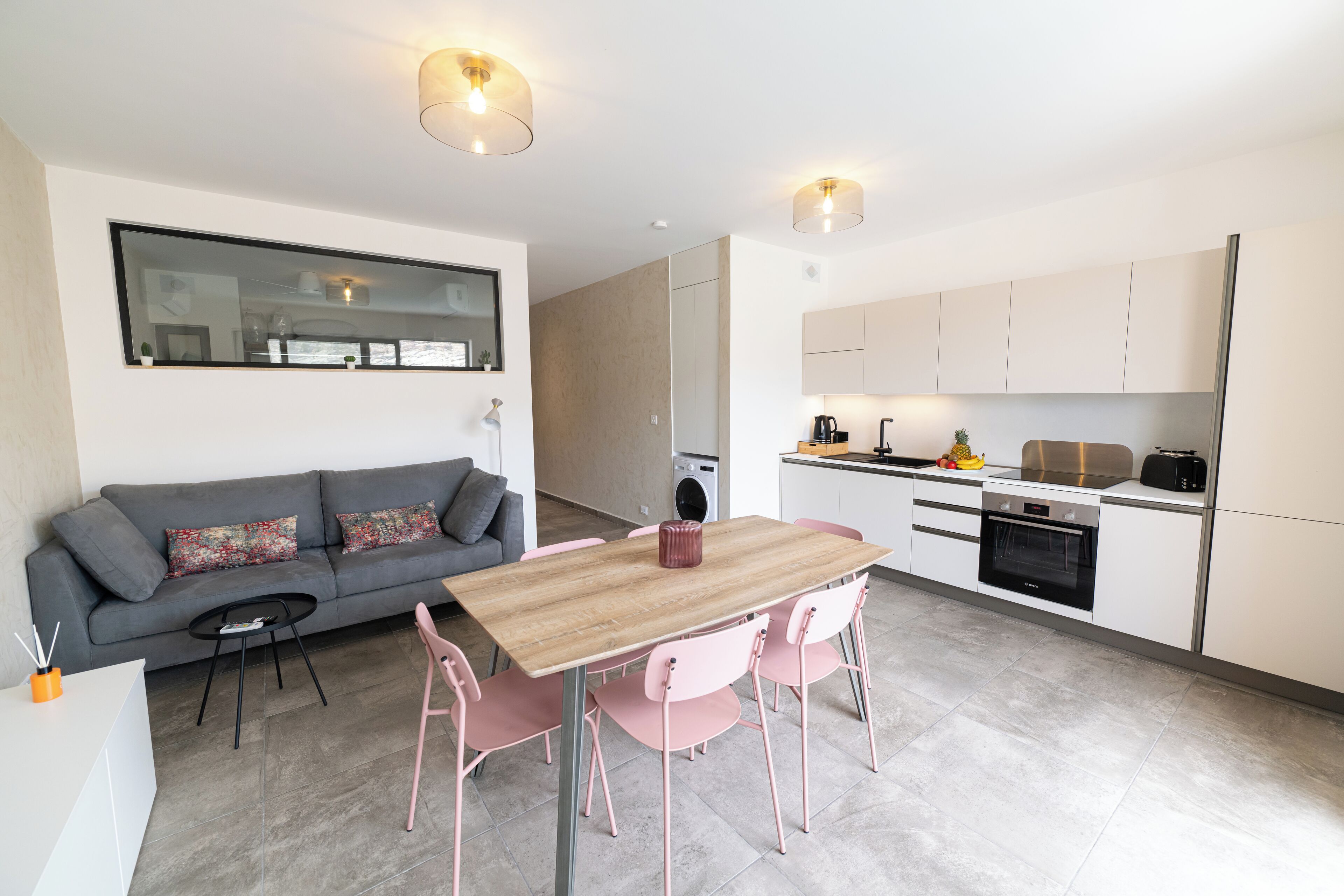 Una cocina moderna con armarios blancos, una mesa de madera y sillas rosas.