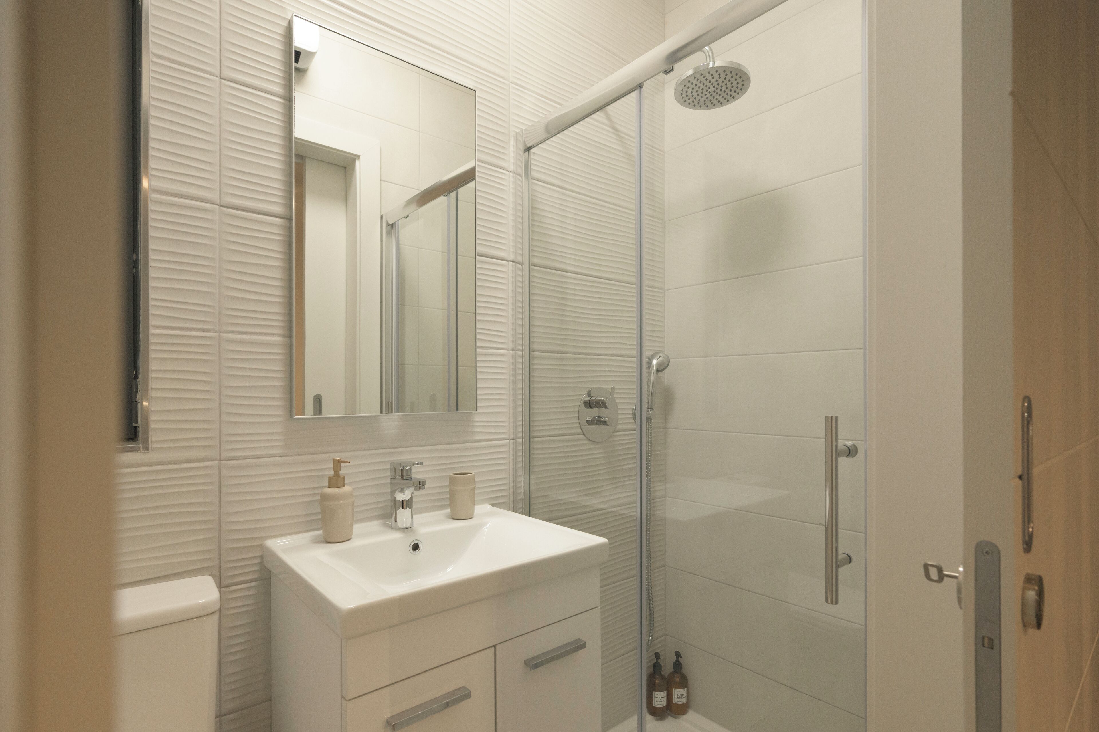 Een badkamer met een witte wastafel, spiegel en een douchecabine van glas.