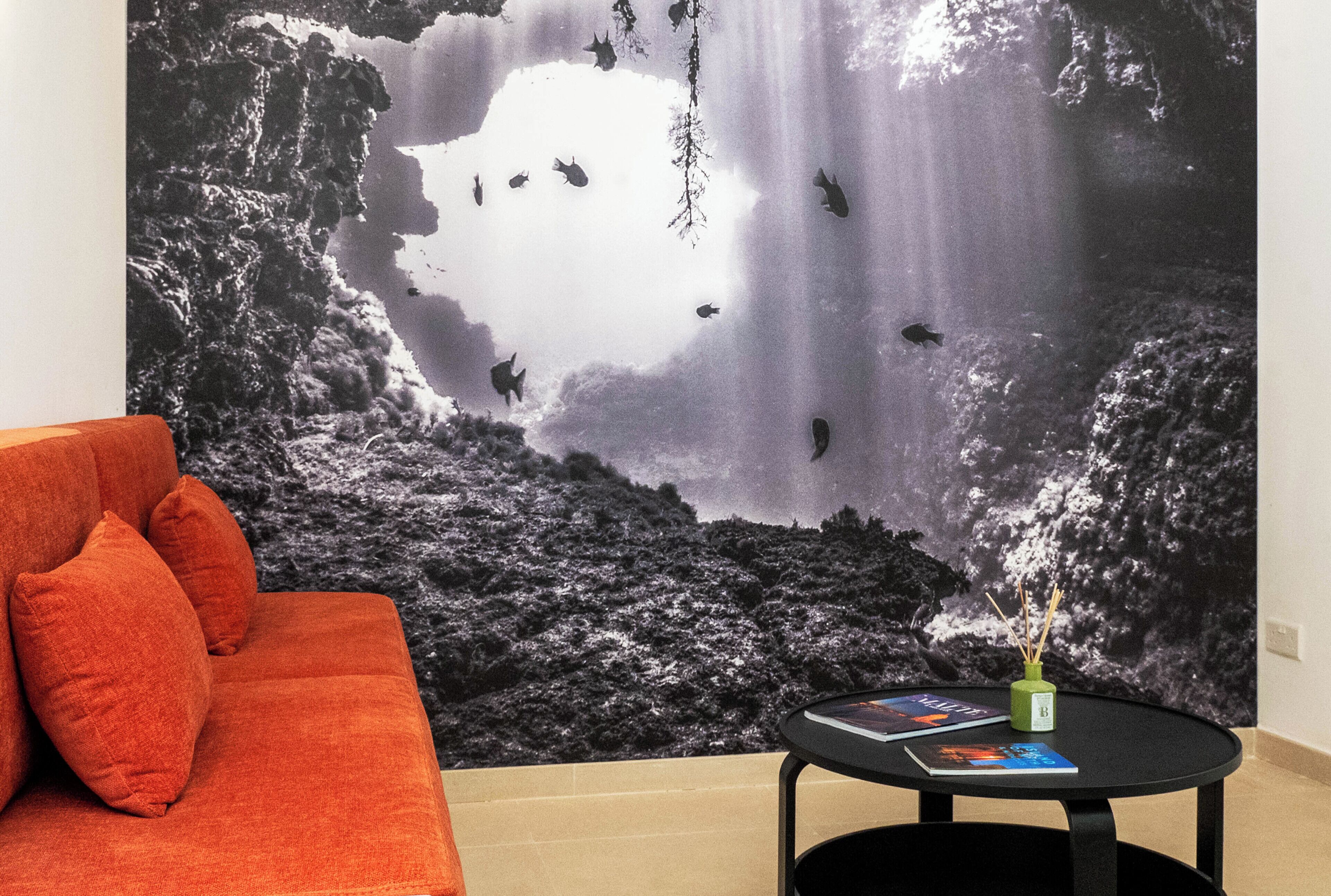 A room with a large wall mural of a waterfall, a red sofa, and a small table with a book and a vase.