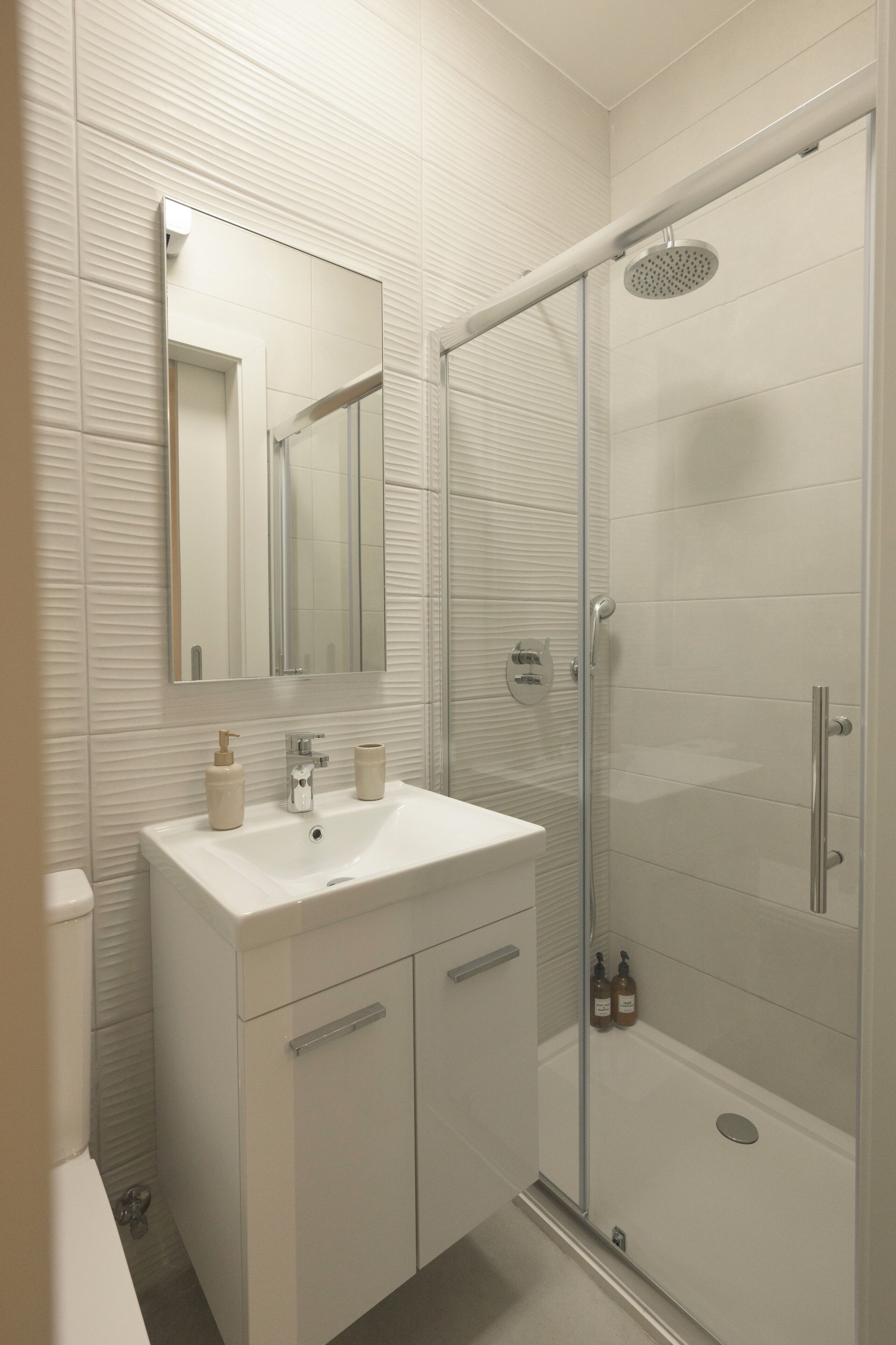 A modern bathroom with a glass-enclosed shower, a white sink, and a large mirror.