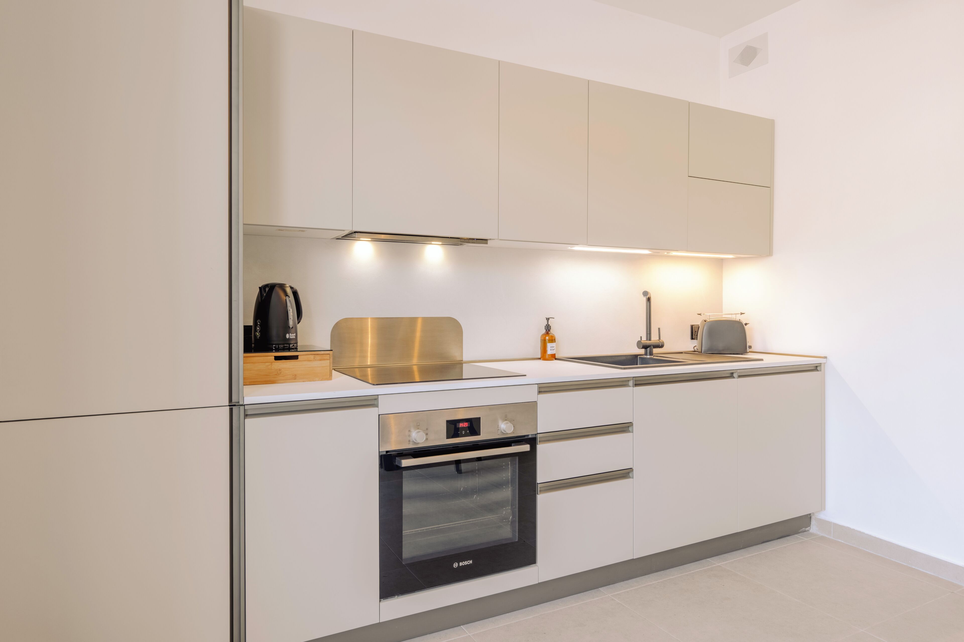 A modern kitchen with white cabinetry, a Bosch oven, a coffee maker, and a kettle.