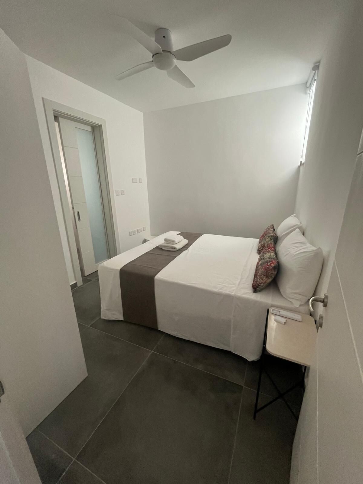Une chambre d’hôtel avec un lit, une table de chevet, un ventilateur de plafond et une porte.