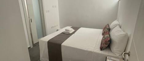 Une chambre d’hôtel avec un lit, une table de chevet, un ventilateur de plafond et une porte.