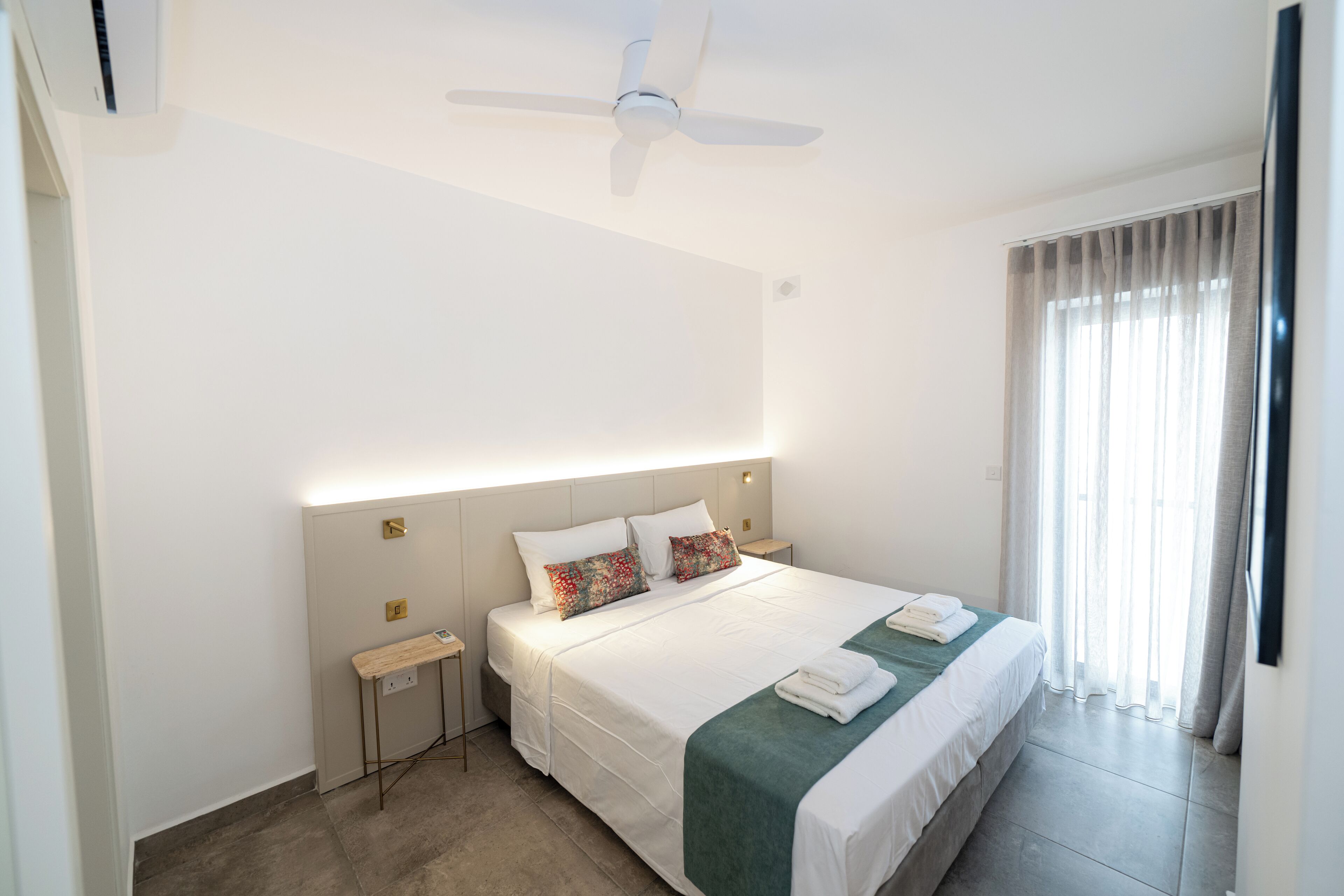 A modern hotel room with a large bed, a ceiling fan, a bedside table, and a window with curtains.
