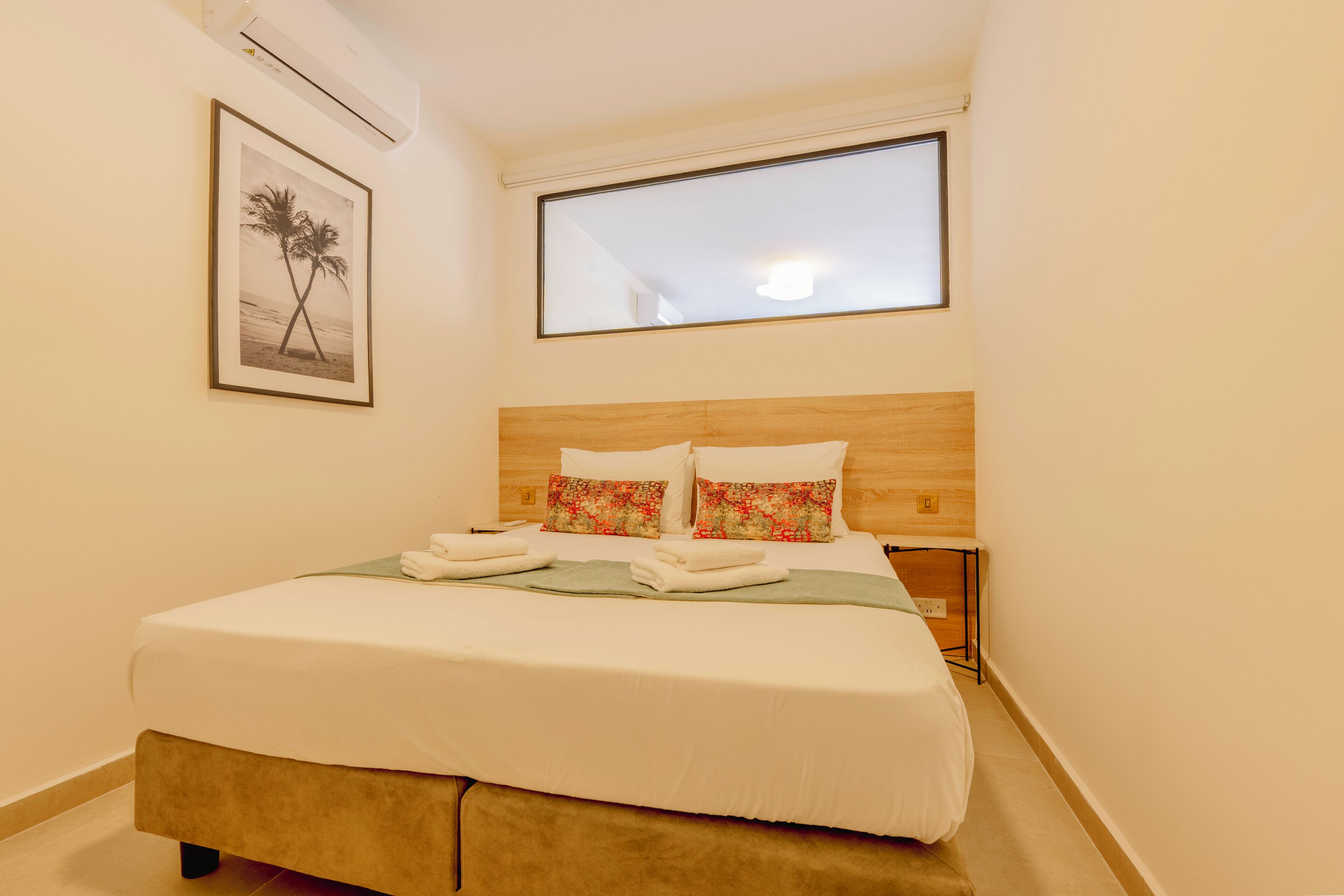 Un letto rifatto con lenzuola bianche e cuscini floreali, un quadro appeso alla parete e una finestra sopra il letto.