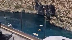 Een zwembadgedeelte met helderblauw water, een rotsachtige klif op de achtergrond en een ligstoel.