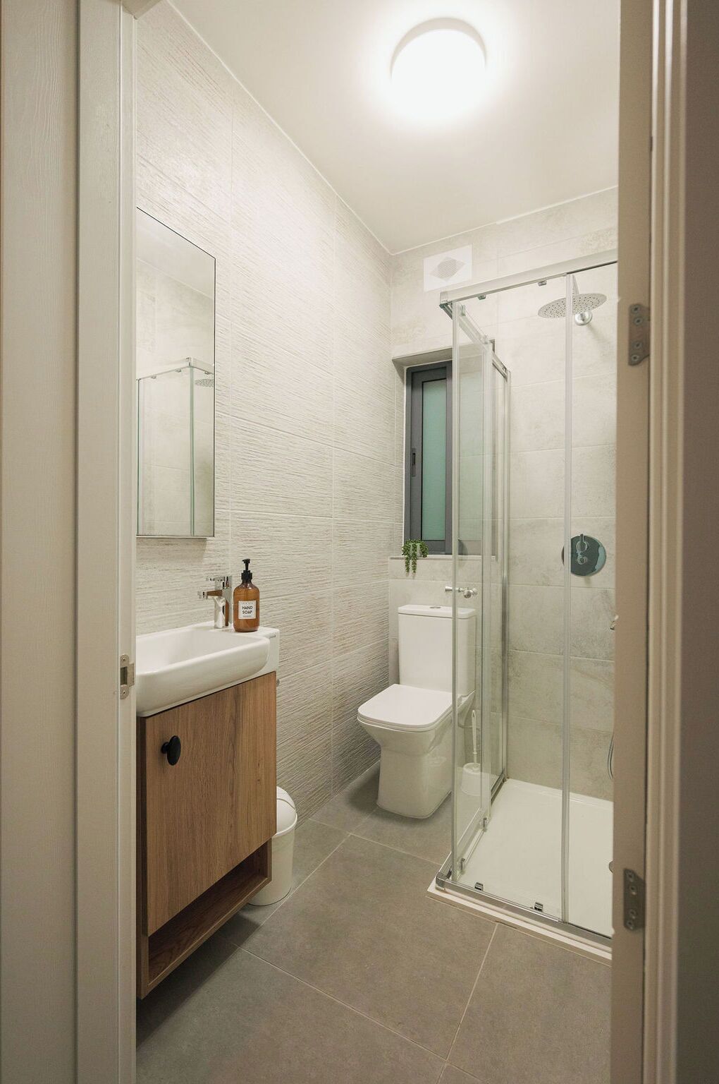 A modern bathroom with a glass shower enclosure, a wooden vanity, and a white toilet.