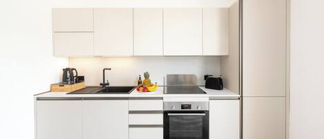 A modern kitchen with white cabinetry, a stainless steel sink, a Bosch oven, and a fruit bowl on the counter.