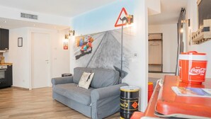 A living room with a sofa, a coffee table, and a wall mural. - VESPA SPRINT APARTMENT Amazing Nature 10' to the beach +PVT Park in City Centre! (Roverano Basso)