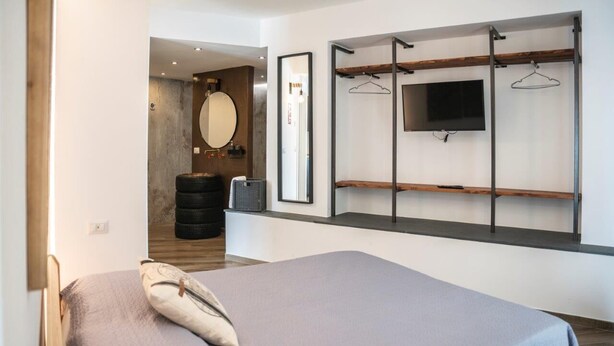 A modern bedroom with a bed, a mounted TV, and a wall-mounted shelf with a hanging rack. - VESPA SPRINT APARTMENT Amazing Nature 10' to the beach +PVT Park in City Centre! (Roverano Basso)