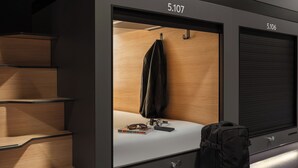 Habitación de hotel moderna con interior de madera, una cama, una maleta y una puerta con la etiqueta 5.107.