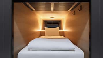 A modern, narrow hotel room with a bed centered in the middle, wooden walls, and a ceiling light fixture.