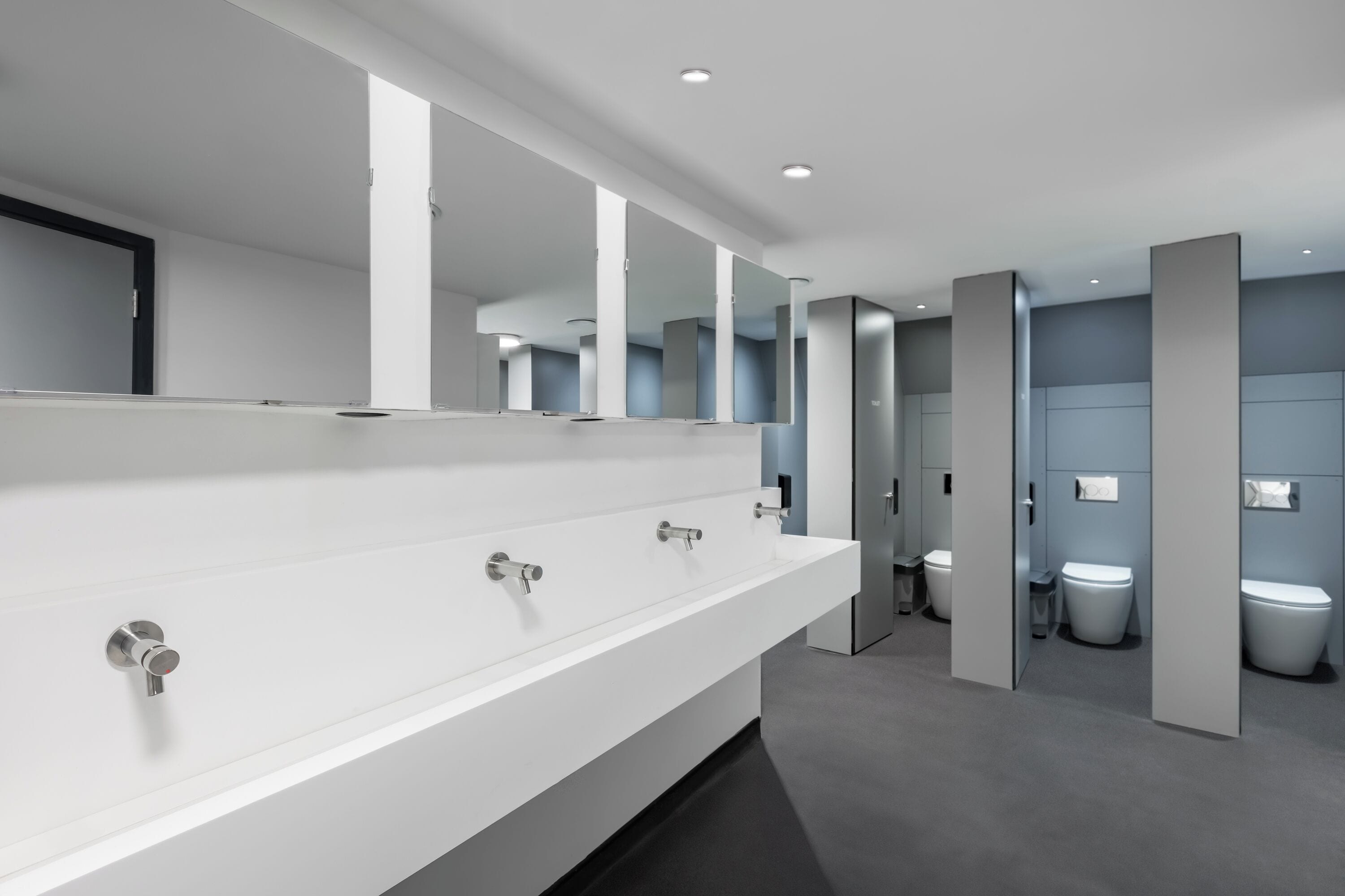 Un baño moderno con un lavamanos blanco alargado, varios espejos y dos inodoros.