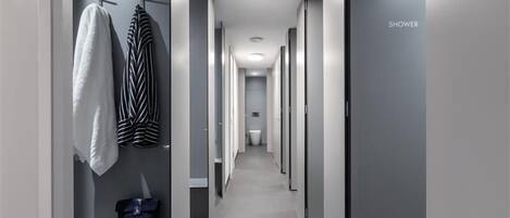 Un pasillo moderno de hotel con zona de ducha, un perchero y un pequeño tocador con un cepillo y una botella.