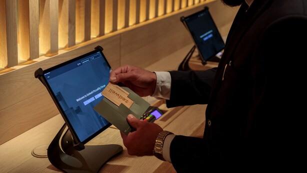 Une personne utilise une tablette sur un comptoir d’accueil, avec un mur en panneaux de bois en arrière-plan.