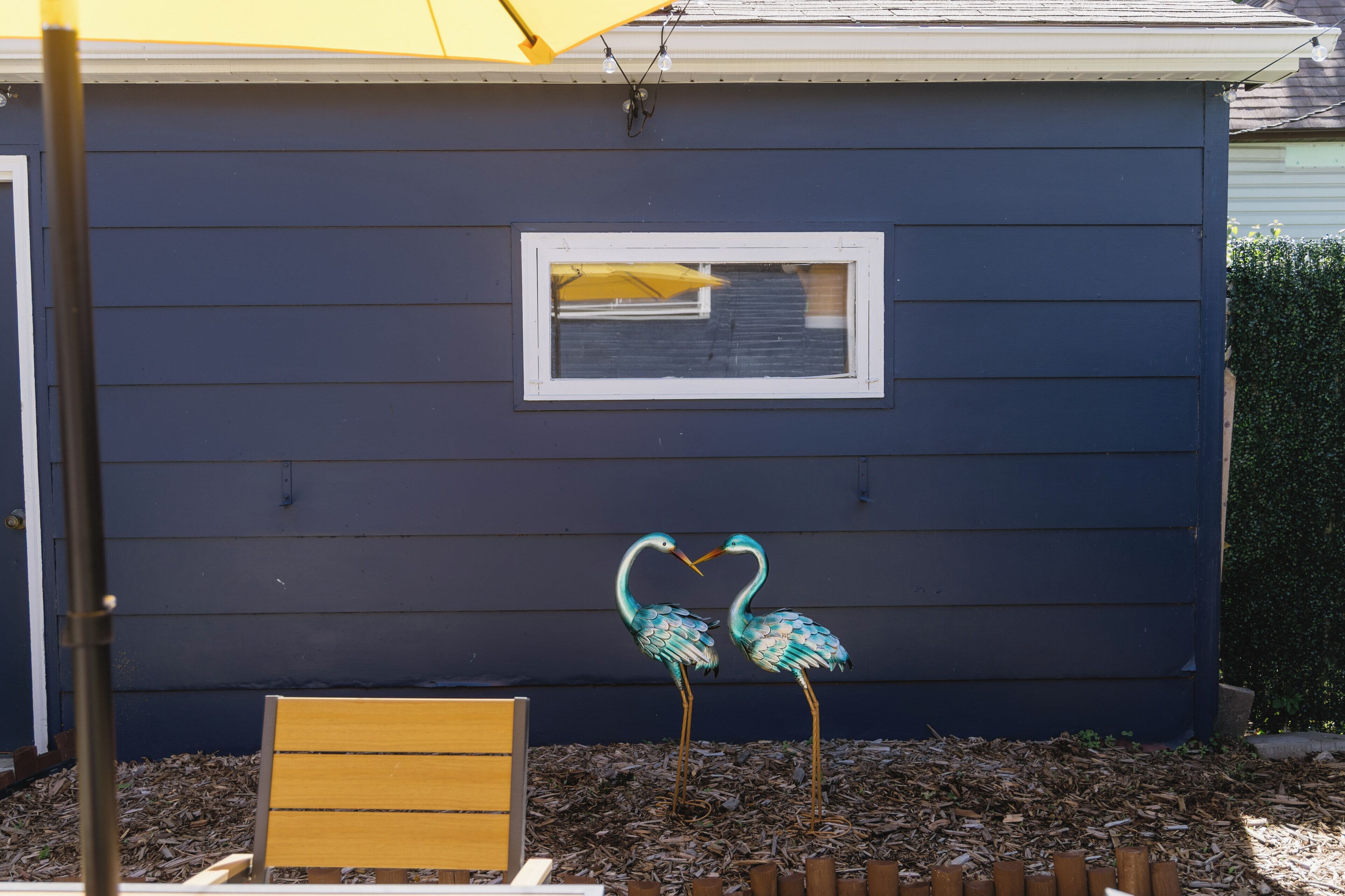 A blue house with a window, a bench, and two decorative bird figures.