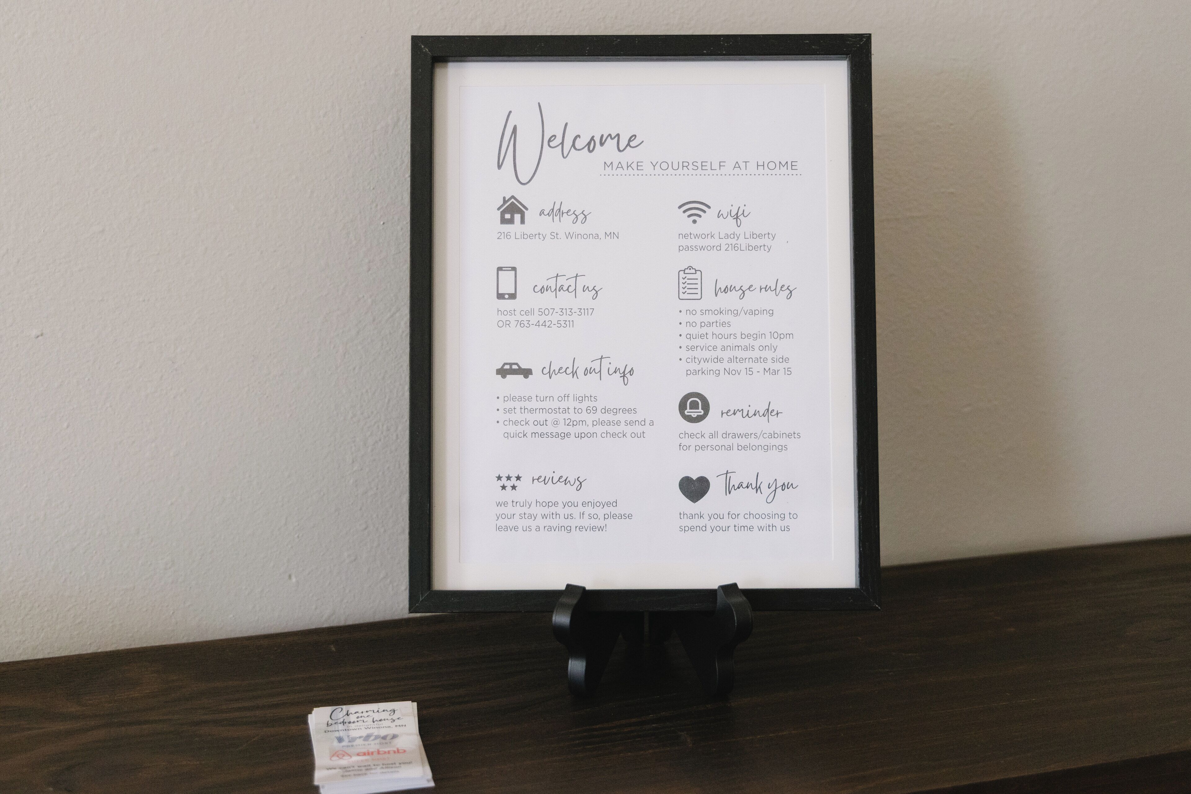 A framed welcome sign with house rules, contact information, and amenities for a home stay.