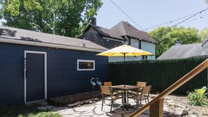 Eine Terrasse mit Tisch und Stühlen, einem gelben Sonnenschirm und einer Holztreppe.