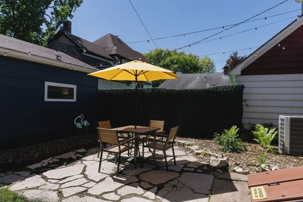 A patio with a table and chairs, a yellow umbrella, and a stone floor.