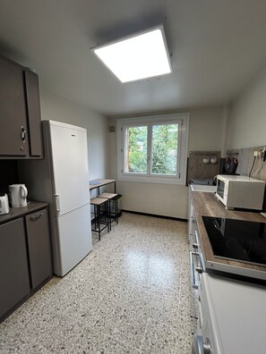 A compact kitchen with a refrigerator, microwave, and stove. There's a window providing natural light and a view of greenery outside.