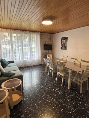 Una habitación con techo de madera, una mesa de comedor con sillas, un sofá y un televisor en la pared.